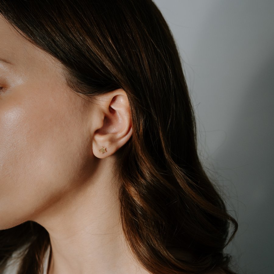 Close-up of a woman's ear wearing a 14K gold star stud earring.