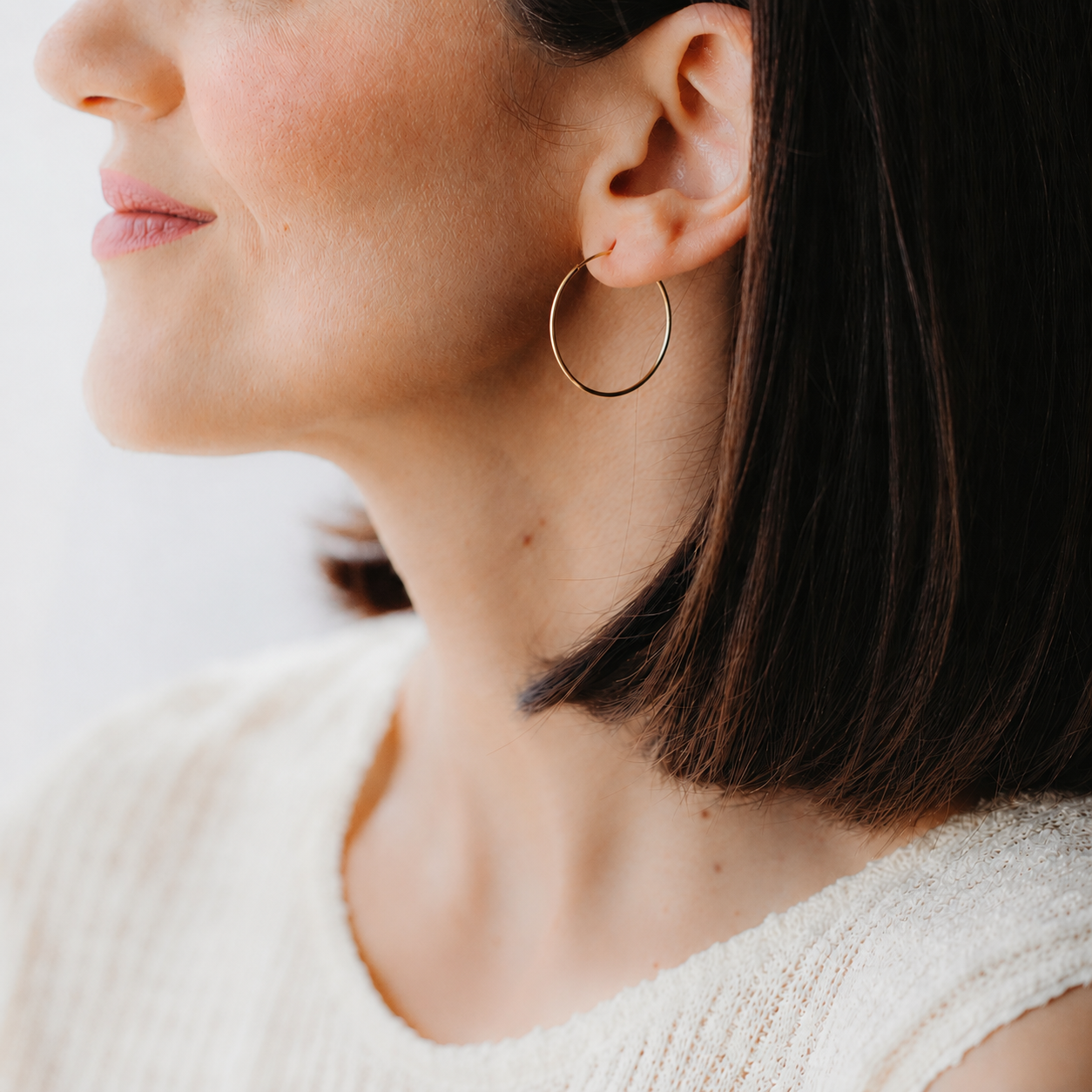 Close-up of a medium 14K yellow gold creole hoop earring worn on the left ear.