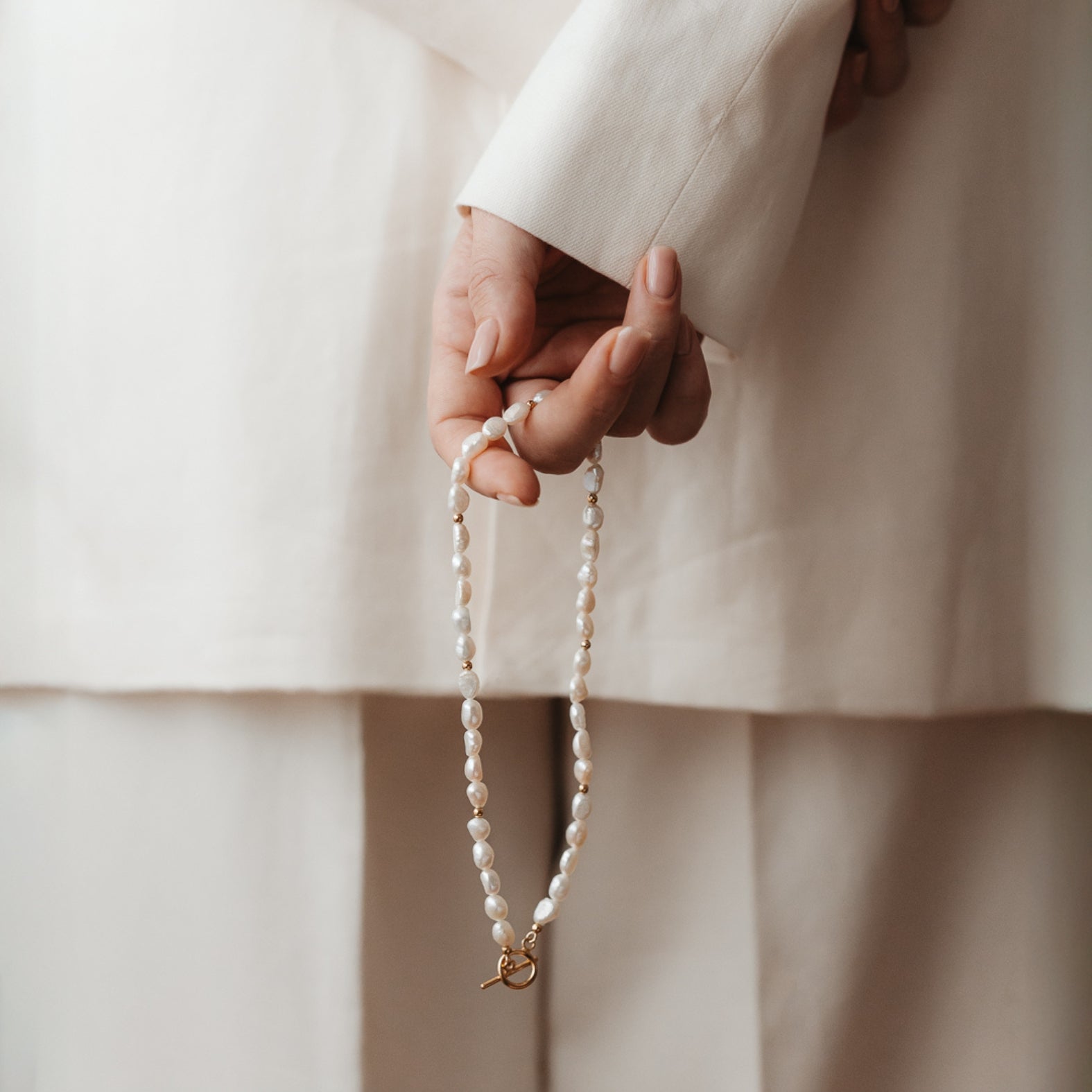 Gros plan d'une main tenant un collier en argent avec des perles naturelles.