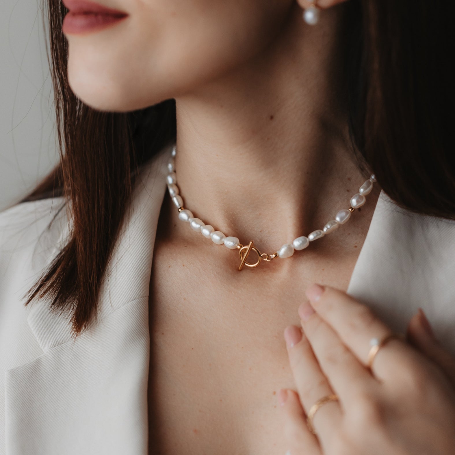Gros plan sur une femme portant un collier en argent avec des perles naturelles et un fermoir en or.