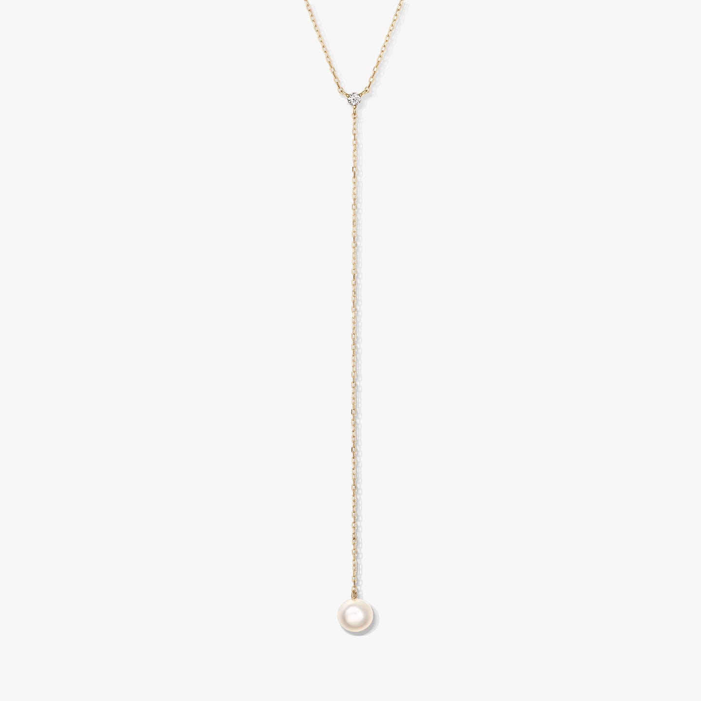 Minimalista arany lariat nyaklánc egyetlen kerek fehér gyöngyfüggővel és apró díszkővel, fehér háttéren középre helyezve.