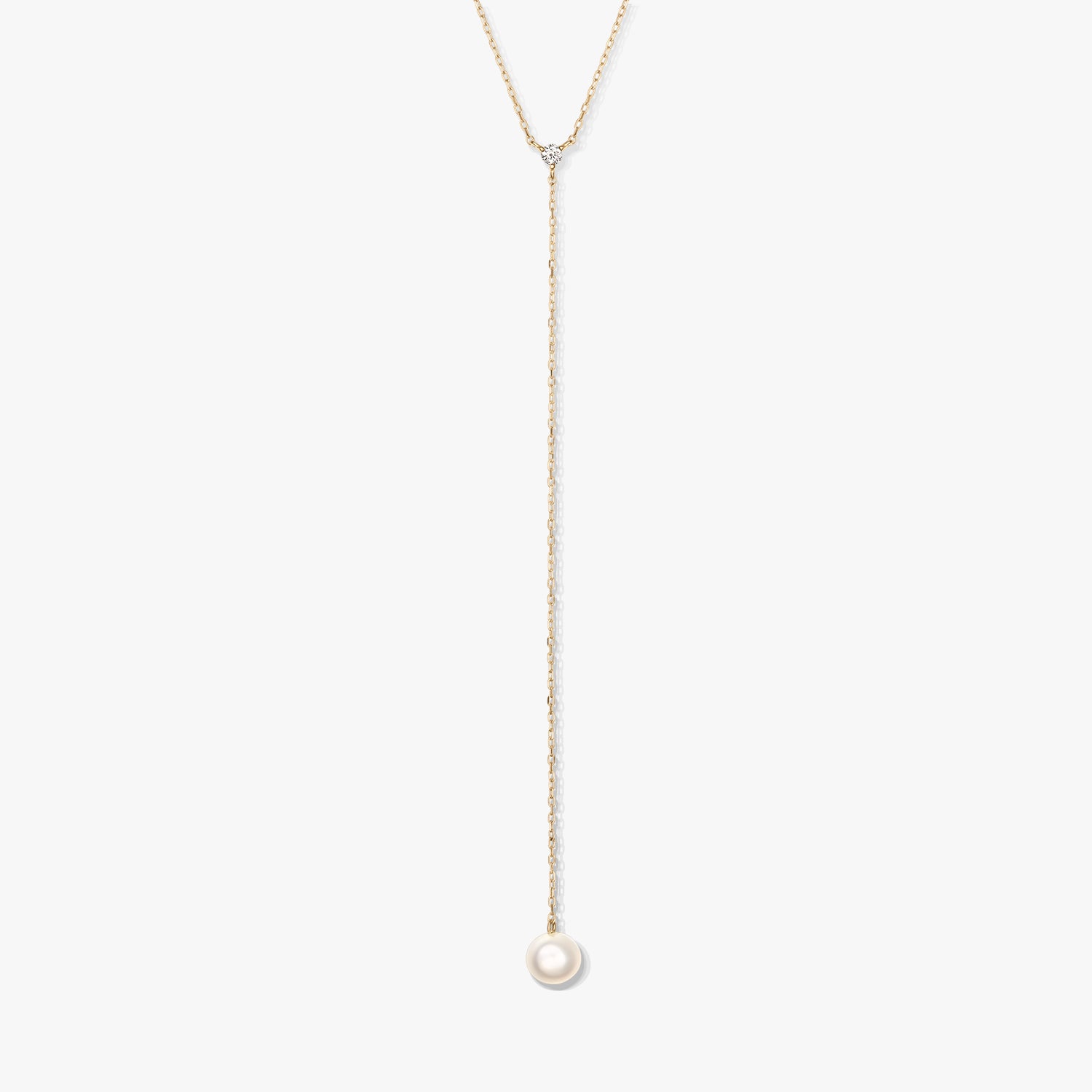 Minimalista arany lariat nyaklánc egyetlen kerek fehér gyöngyfüggővel és apró díszkővel, fehér háttéren középre helyezve.