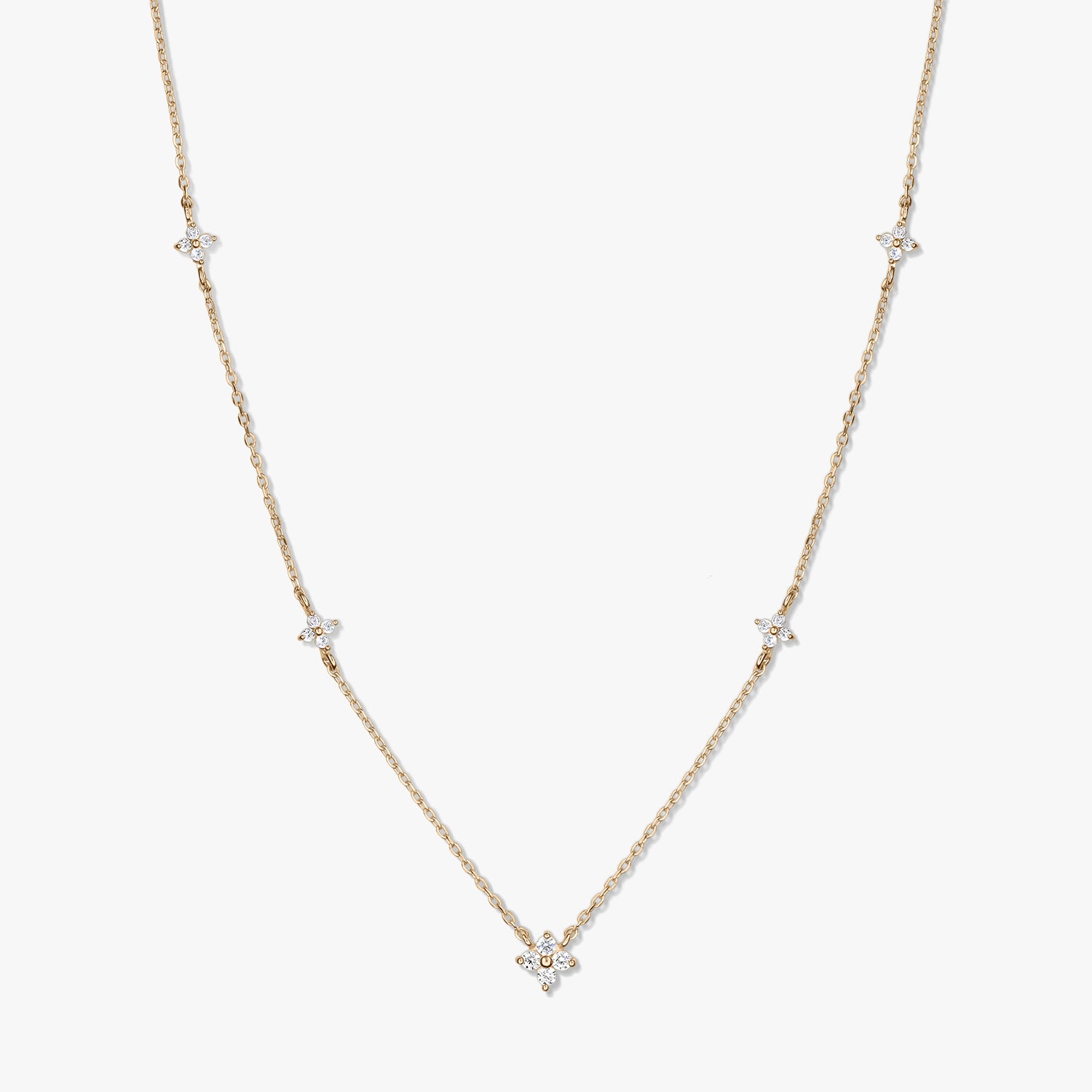 Delicate 14K yellow gold station necklace featuring small white zirconia clover motifs on a fine chain, photographed against a white background.