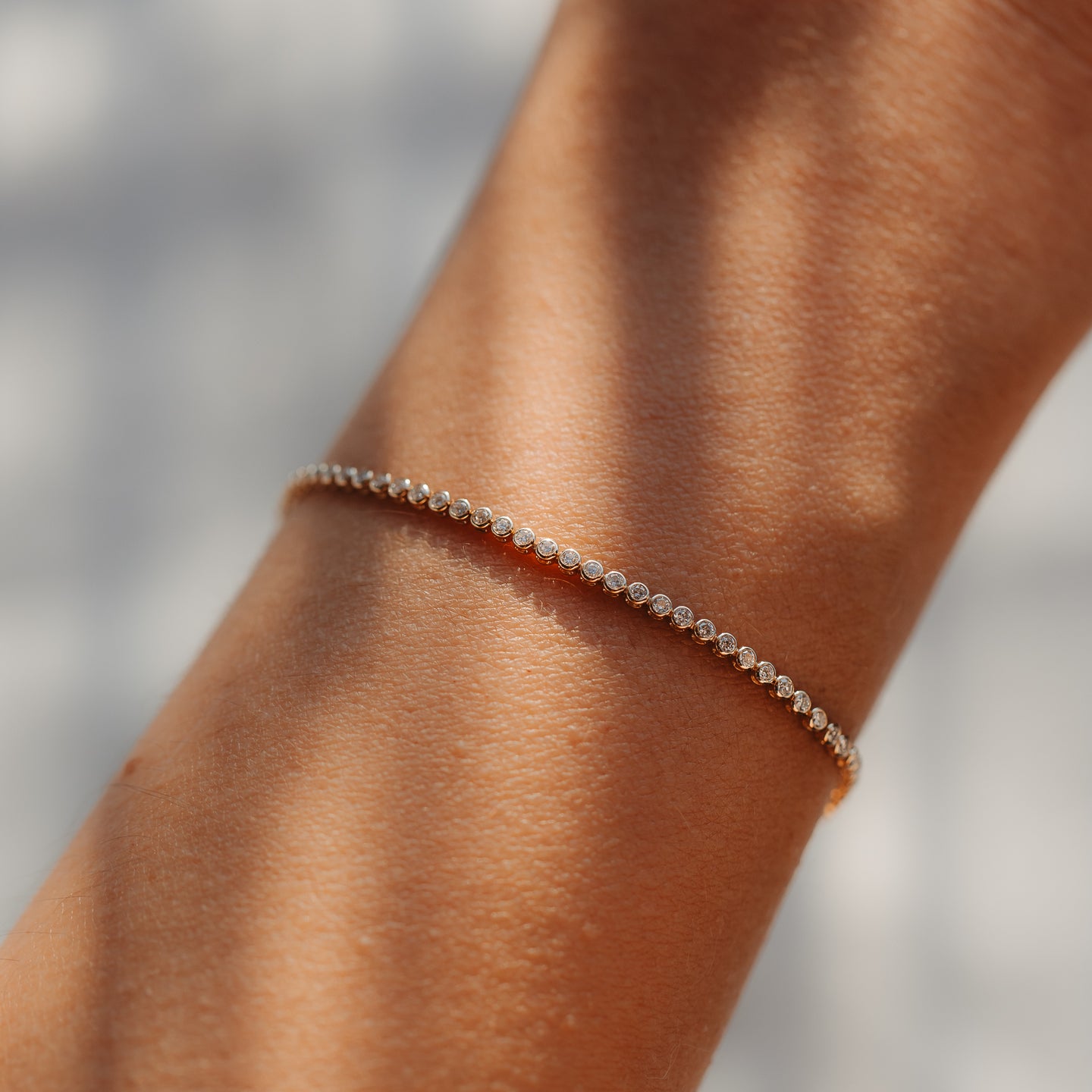 Gros plan d'un bracelet tennis raffiné en or jaune 14K, serti de petits diamants ronds, porté au poignet et baigné d'une douce lumière naturelle.