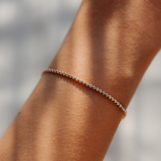 Close-up of a delicate 14K yellow gold tennis bracelet adorned with small round diamonds on the wrist, bathed in soft natural light.
