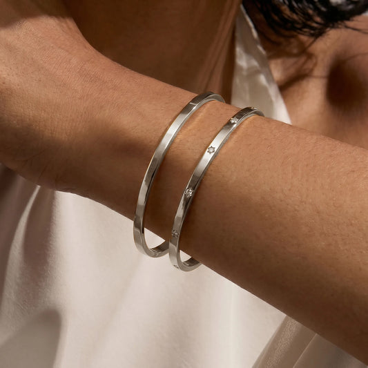 Gros plan sur un poignet orné de deux bracelets en argent minimalistes. L'un est simple et l'autre est orné de petites pierres de zirconium.