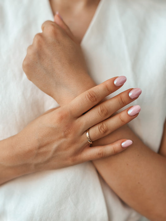Close-up of a hand adorned with a wide rounded gold wedding band, complemented by pink and silver nail art.