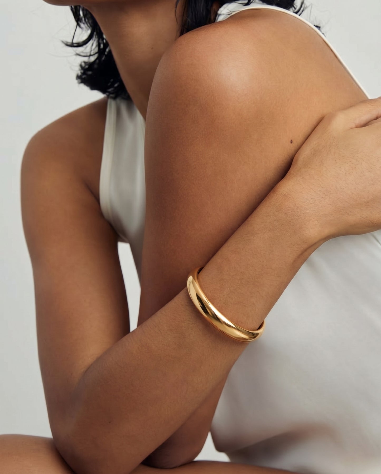 Close-up of a person wearing a gold-plated bangle bracelet on their arm against a white background.