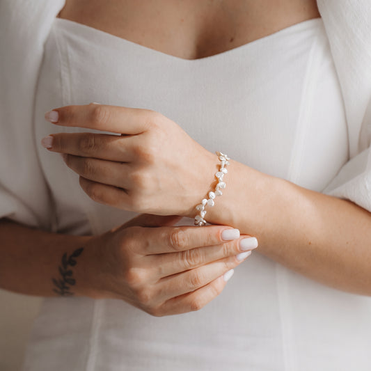 Gros plan sur des mains portant un bracelet en argent sterling plaqué or, orné de perles keshi blanches, sur fond d’une robe blanche.