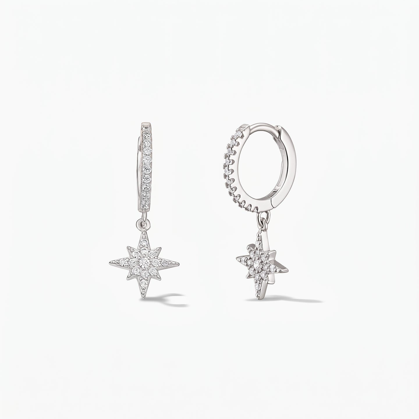 Paire de créoles huggie en argent sterling 925 avec pendentifs Étoile du Nord pavés d'oxydes de zirconium blancs, sur fond blanc.