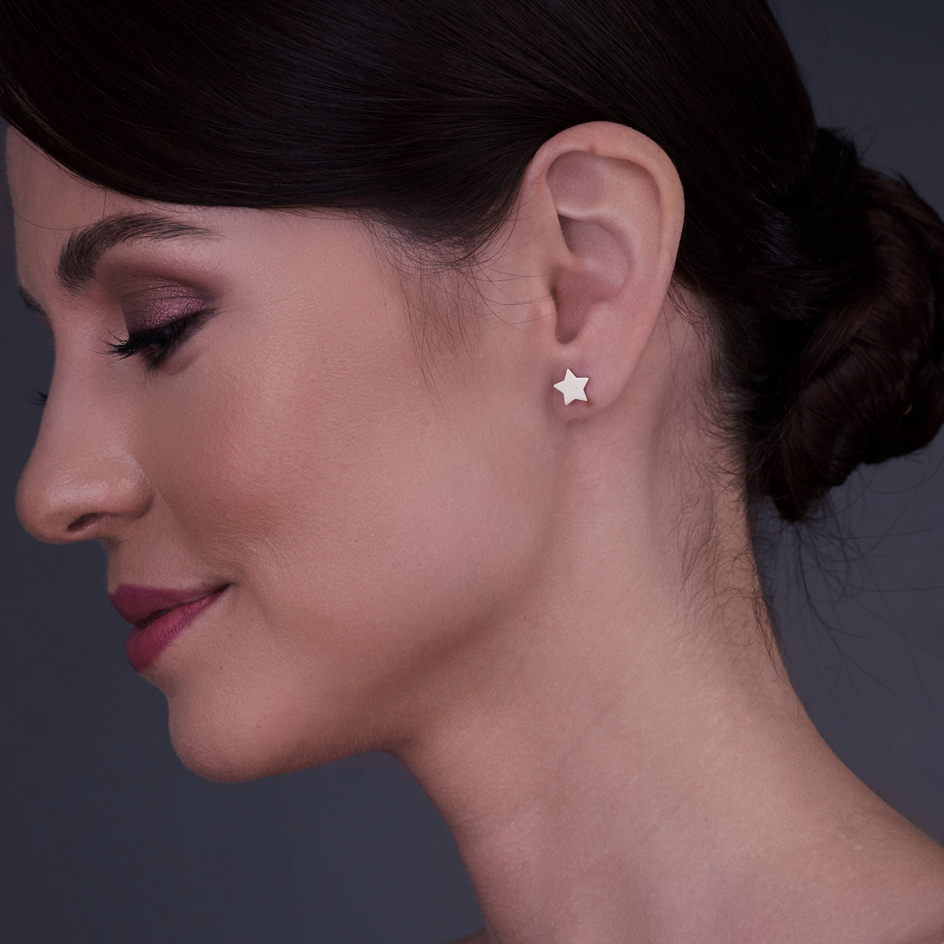 Profile view of a woman wearing 14K gold star-shaped earrings.