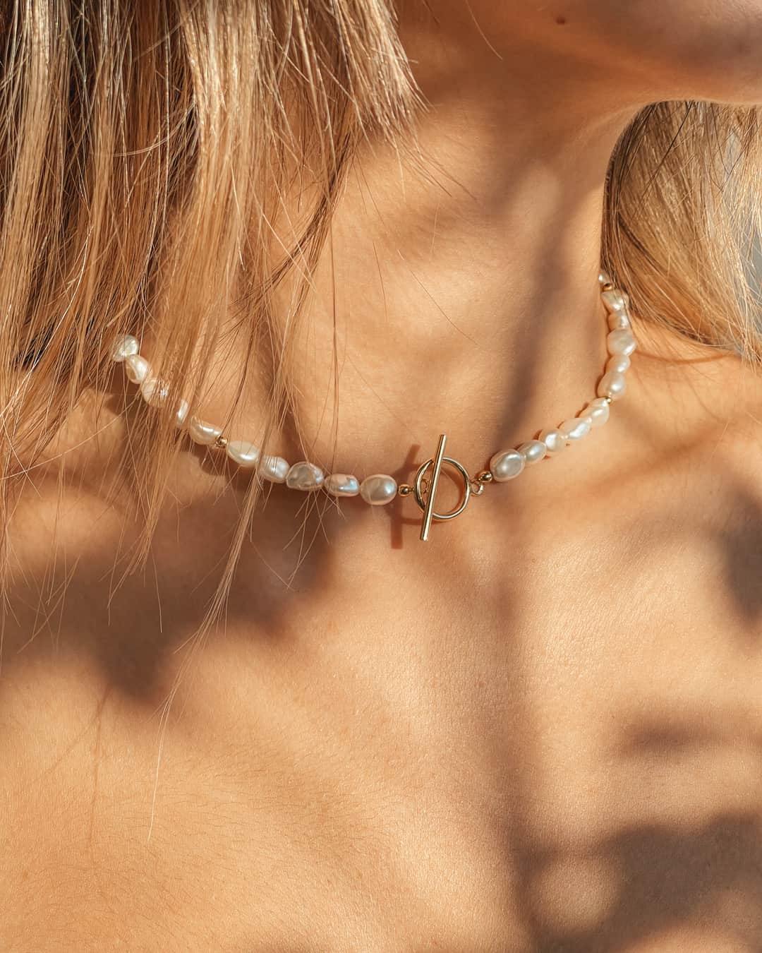 Gros plan sur le cou d'une femme portant un collier en argent avec des perles naturelles et un fermoir en or.