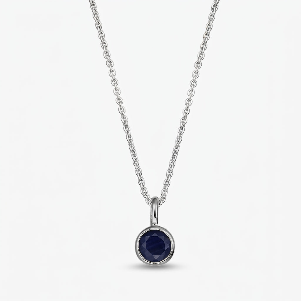 Elegant sterling silver birthstone necklace with a small round bezel‑set dark blue sapphire pendant on a fine chain, isolated on white.