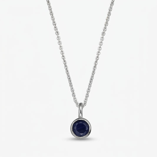 Elegant sterling silver birthstone necklace with a small round bezel‑set dark blue sapphire pendant on a fine chain, isolated on white.