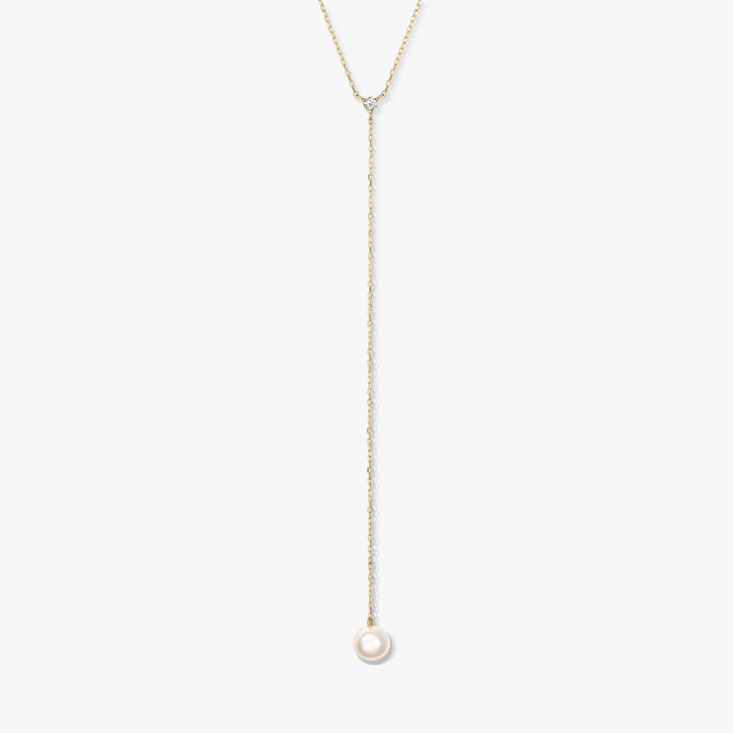 Minimalista arany lariat nyaklánc egyetlen kerek fehér gyöngyfüggővel és apró díszkővel, fehér háttéren középre helyezve.