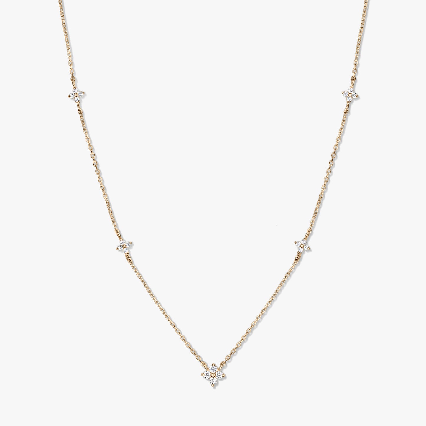 Delicate 14K yellow gold station necklace featuring small white zirconia clover motifs on a fine chain, photographed against a white background.
