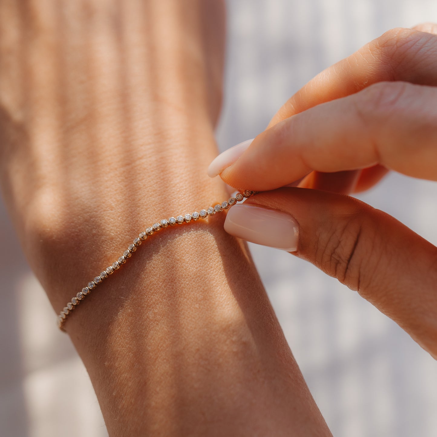 Gros plan d'une main qui attache un bracelet tennis en diamants en or jaune 14K autour d'un poignet, à la lumière chaude du soleil.