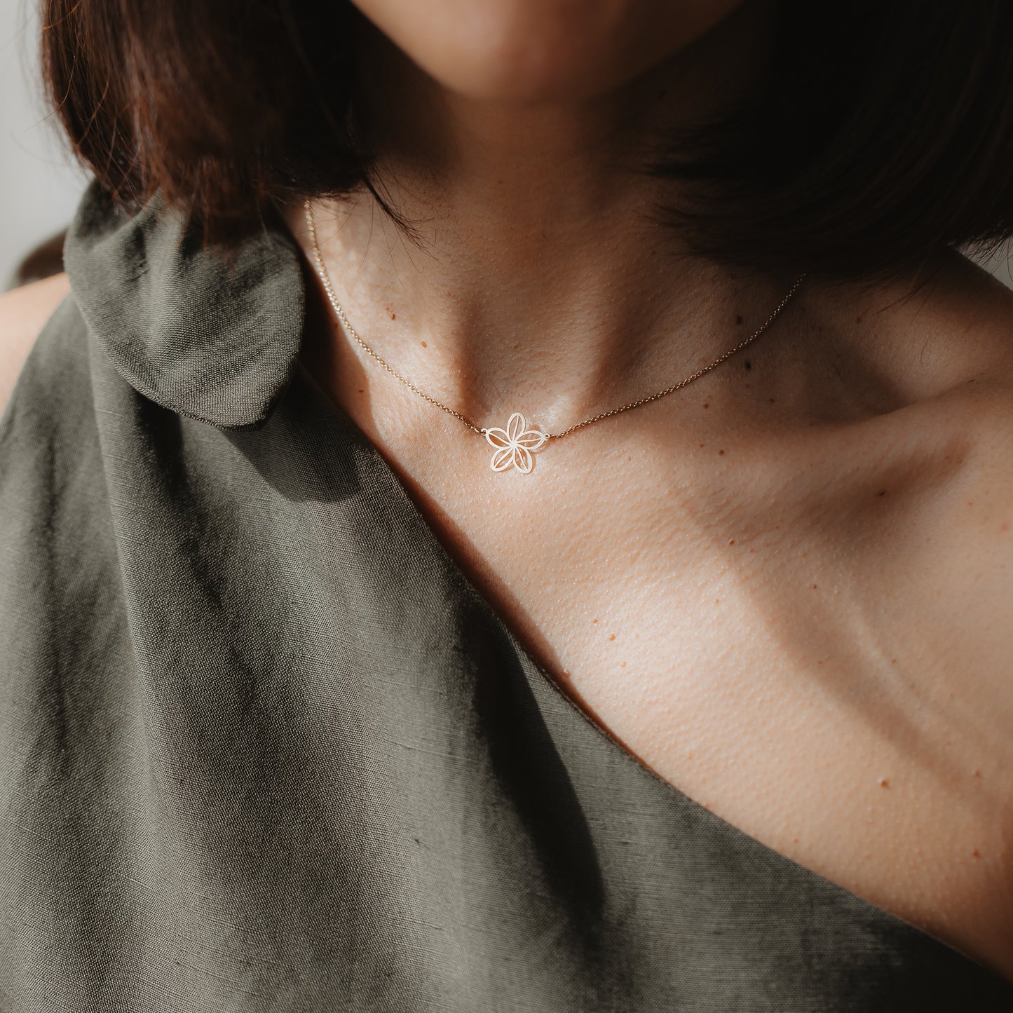 Close-up of a model wearing the Wildflower 14K yellow gold necklace with a delicate flower outline pendant, shown at the collarbone in natural light.
