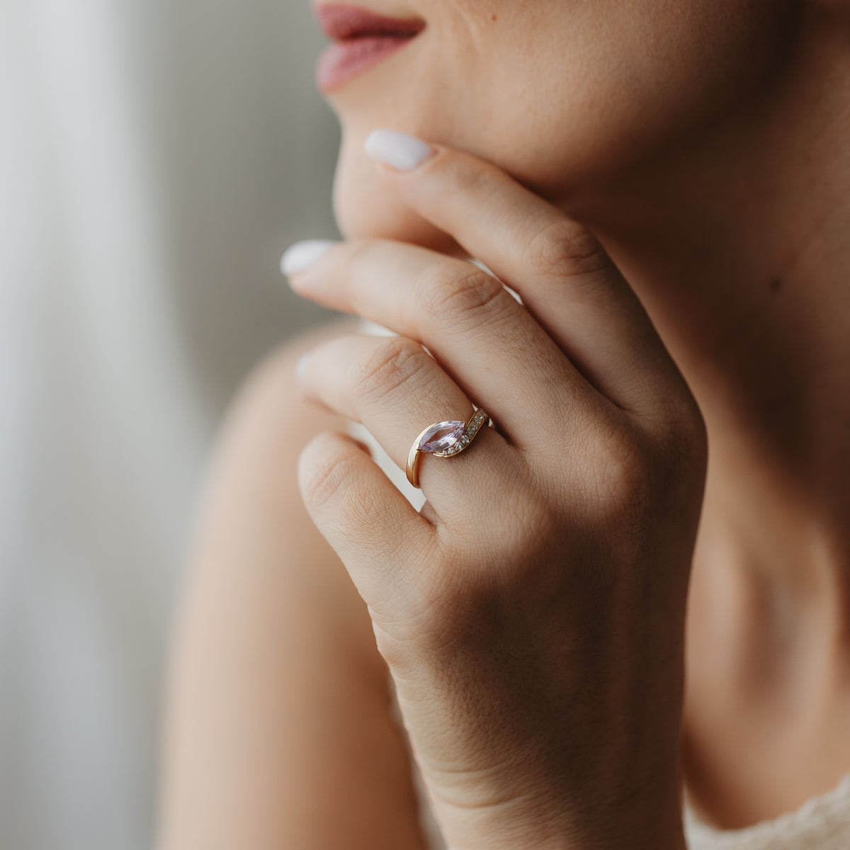 Közeli felvétel egy kézről az arc közelében, amelyen a Velvet Rose 14K sárga arany gyűrű látható marquise csiszolású rózsaszín zafírral és apró kísérő gyémántokkal.