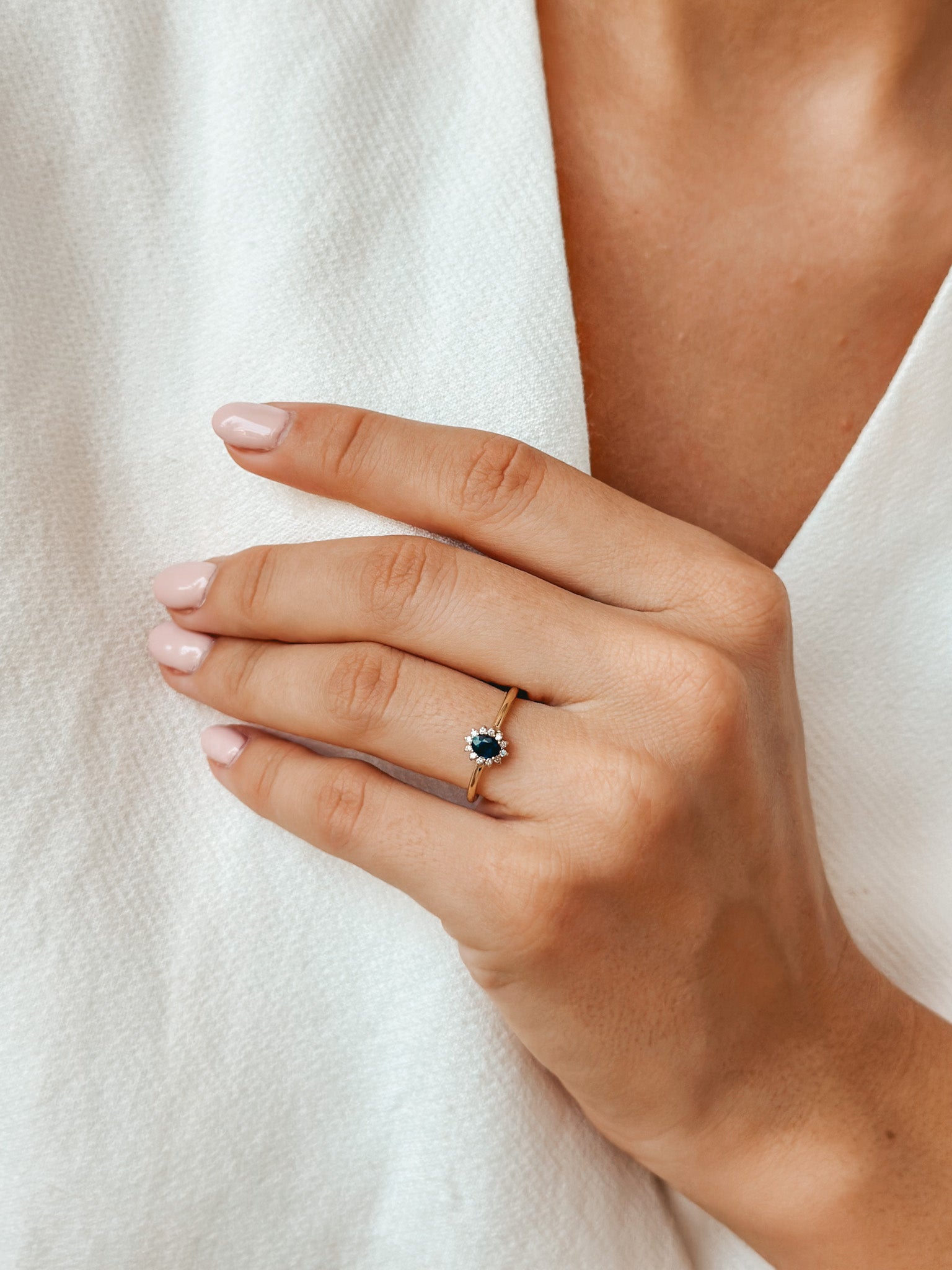 Close-up of a hand adorned with a gold ring featuring a sapphire and diamonds