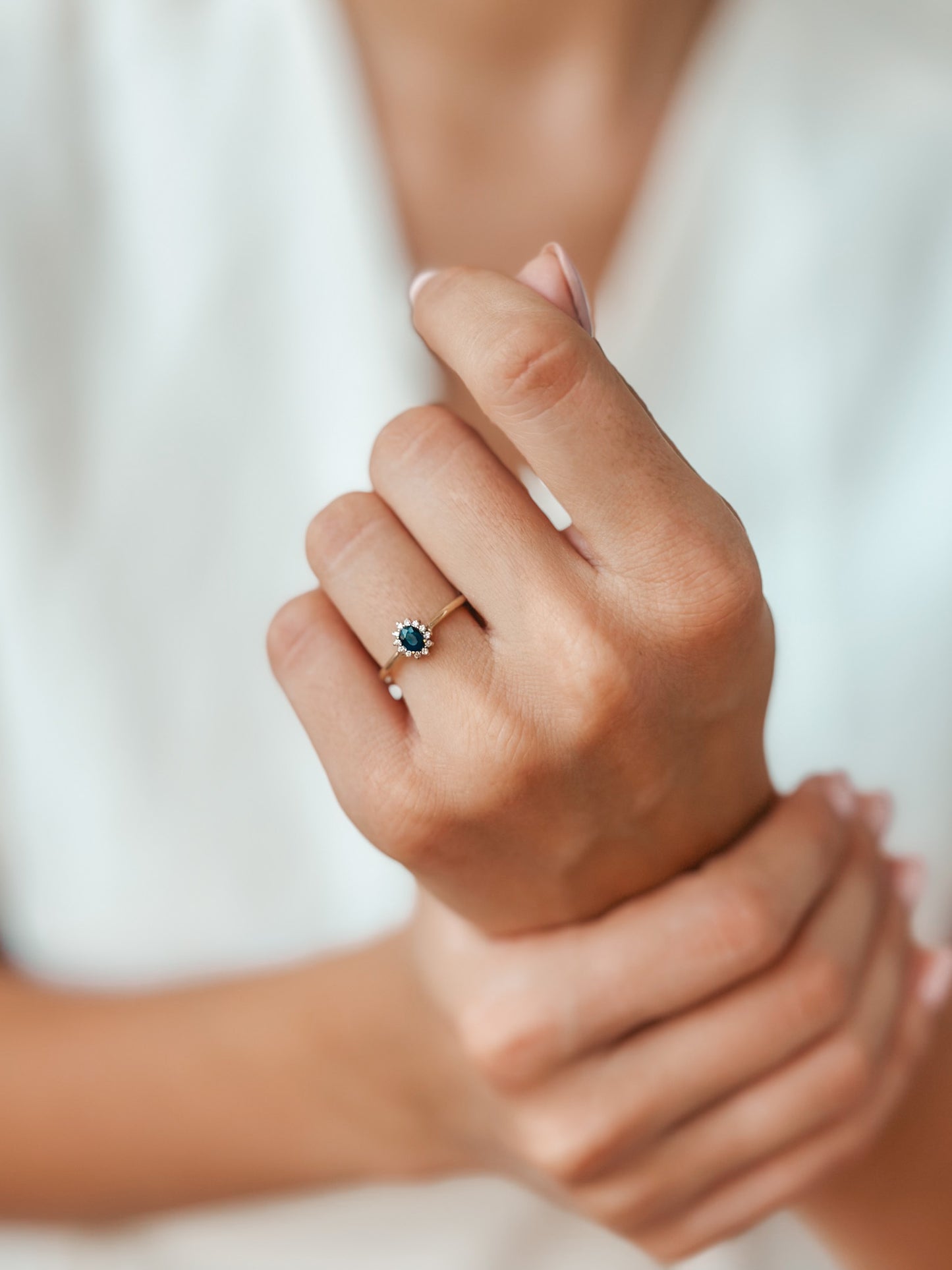 Close-up of a hand wearing a Genn Gold Ring with sapphire and diamonds.