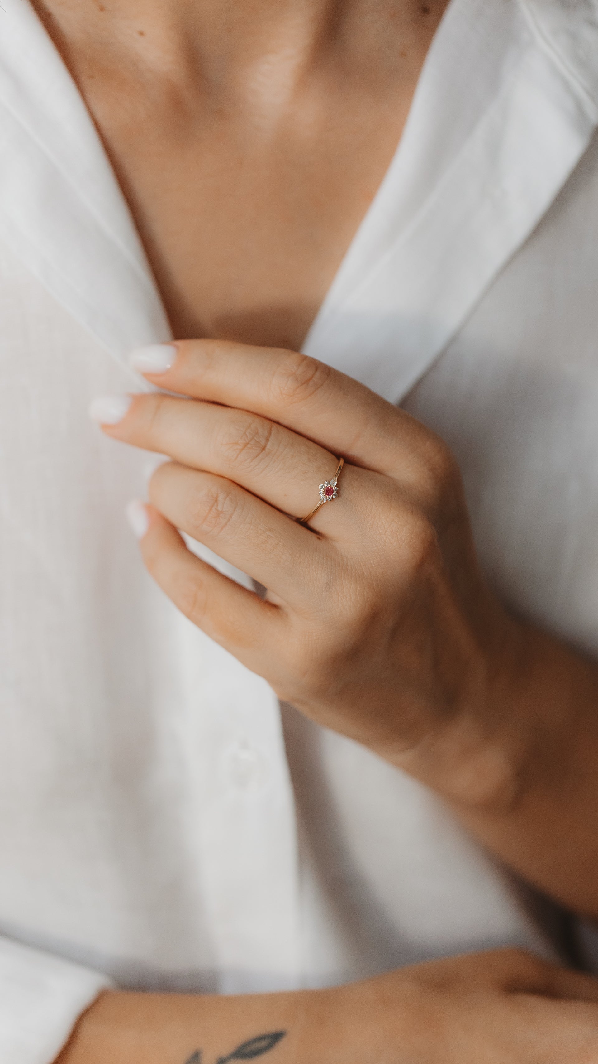 Gros plan d'une main portant une bague délicate en or jaune, sertie d'une tourmaline rose au centre et d'un halo de saphirs blancs.