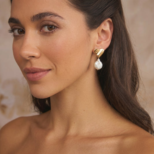 Close-up of a woman wearing a gold-plated silver earring with a heart shape and a dangling natural pear shaped stone.