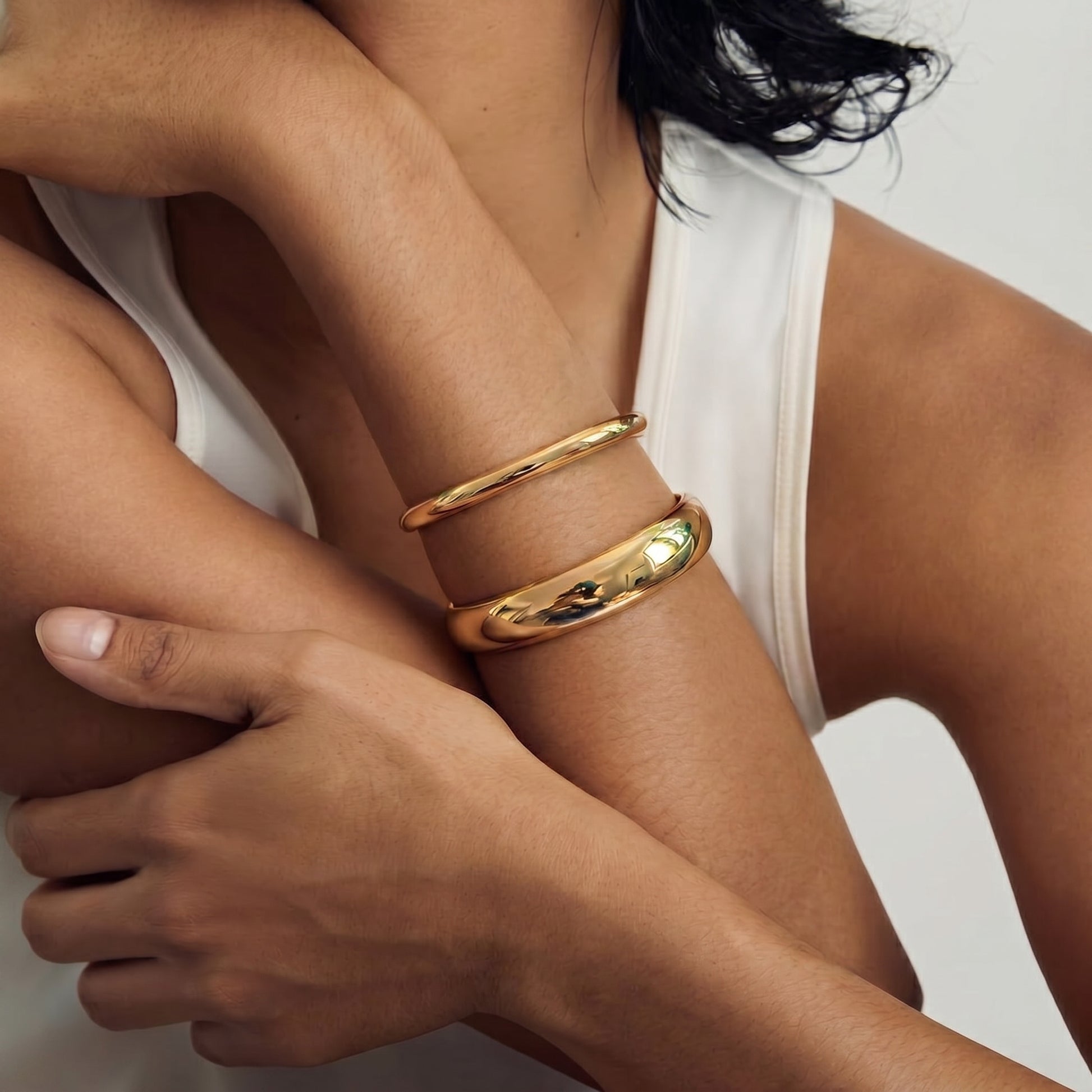 Close-up of two golden bracelets worn on a person's arm, showcasing a minimalist design against a neutral background.