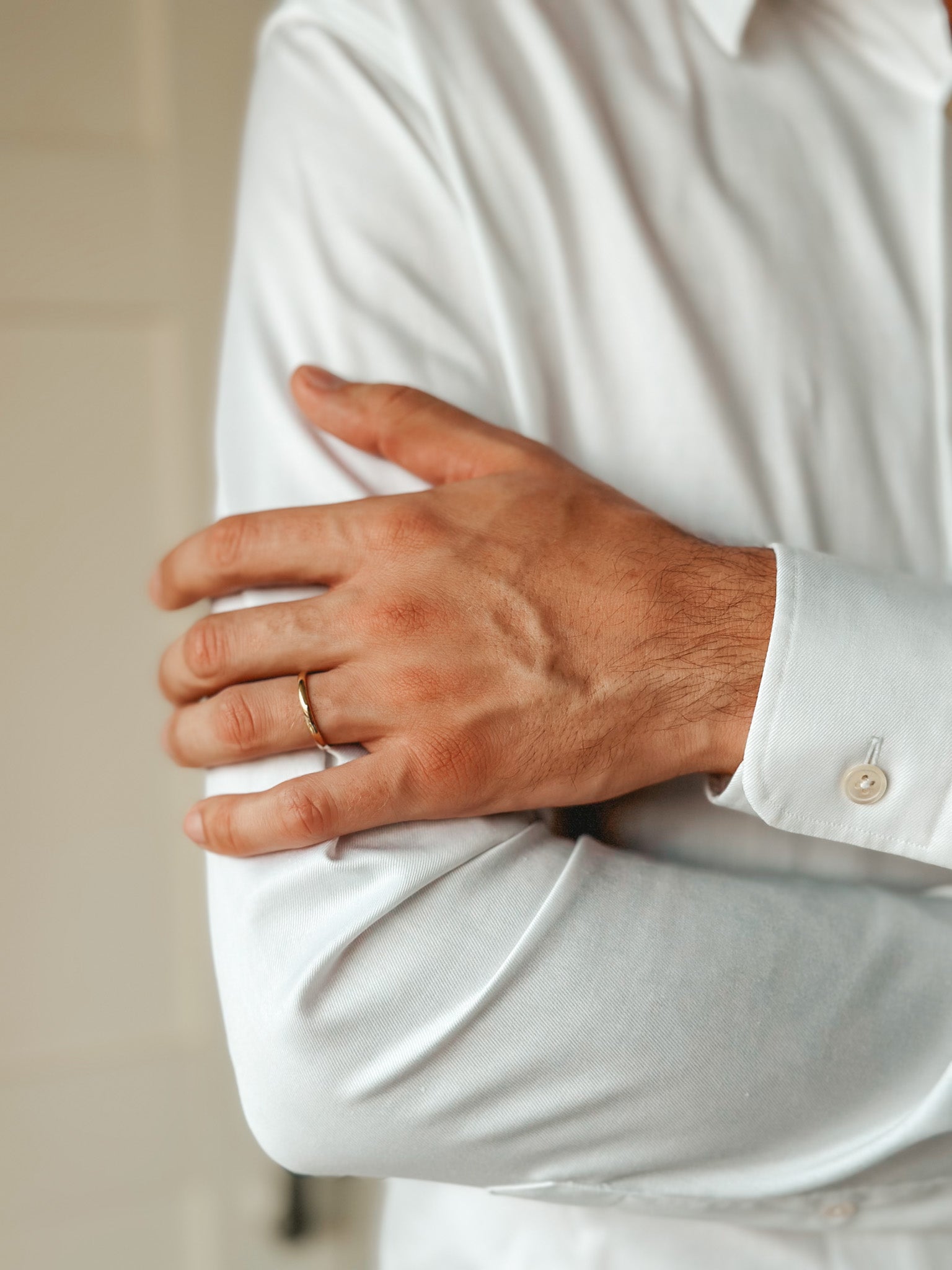 Gros plan sur une personne portant une chemise blanche et une fine alliance en or à son doigt.