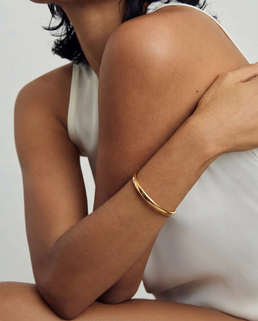 Close-up of a person wearing a gold and silver bracelet on their arm, dressed in a white sleeveless top.