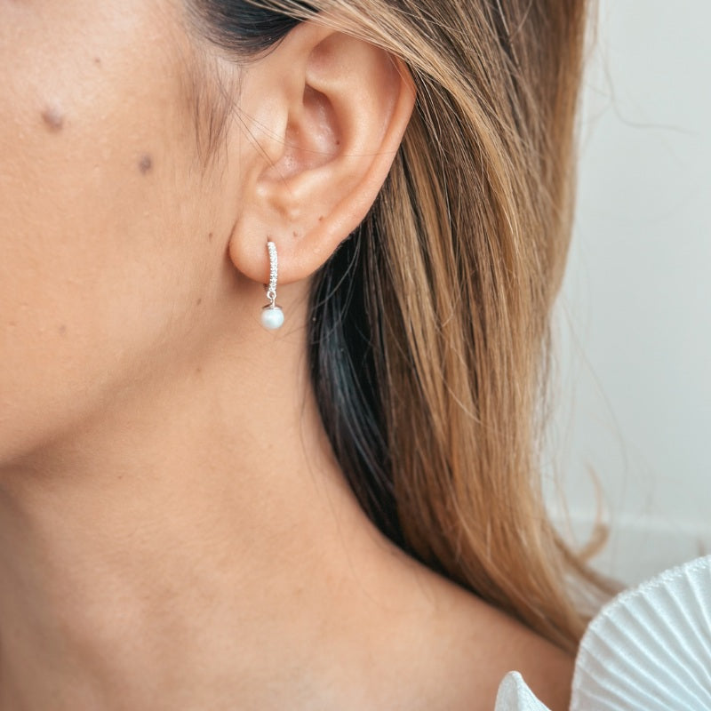 Close-up of a woman's ear wearing silver earrings with a pearl and zirconia design.