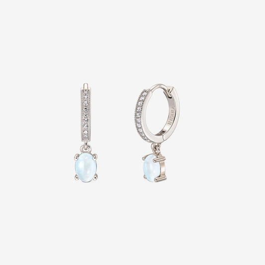 Paire de boucles d’oreilles huggie en argent sterling avec faces pavées et pendentifs en pierre de lune cabochon ovale sur fond blanc.