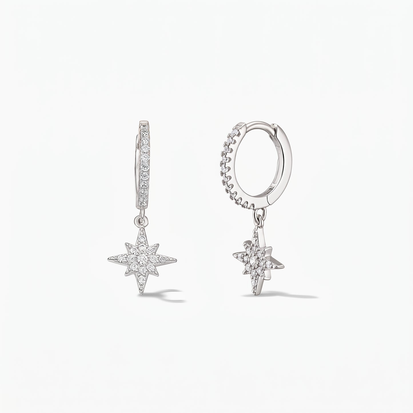 Paire de créoles huggie en argent sterling 925 avec pendentifs Étoile du Nord pavés d'oxydes de zirconium blancs, sur fond blanc.