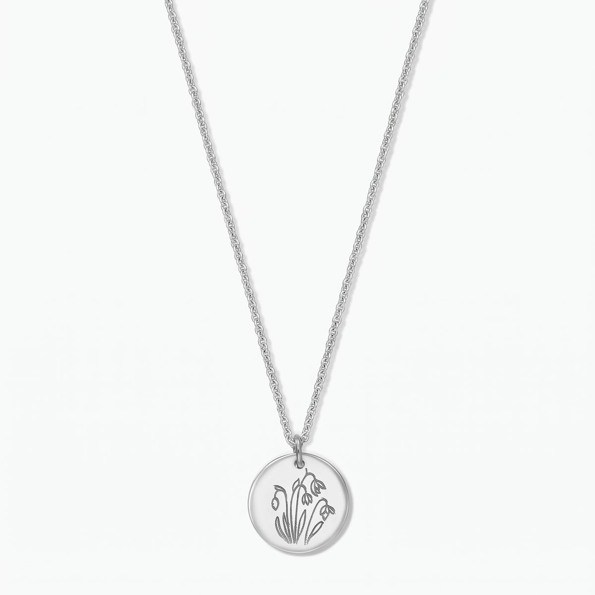 Collier fleur de naissance en argent sterling avec un pendentif disque rond gravé de perce-neige de janvier sur une chaîne fine, isolé sur fond blanc.