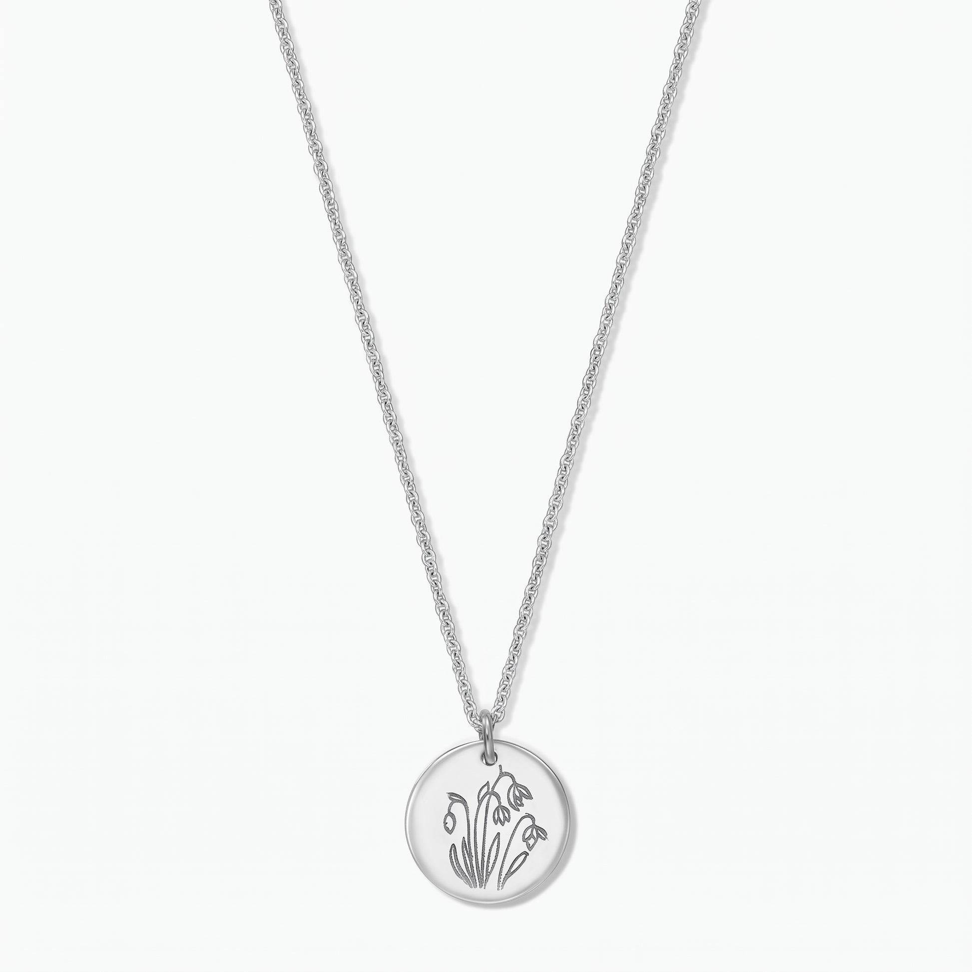 Collier fleur de naissance en argent sterling avec un pendentif disque rond gravé de perce-neige de janvier sur une chaîne fine, isolé sur fond blanc.