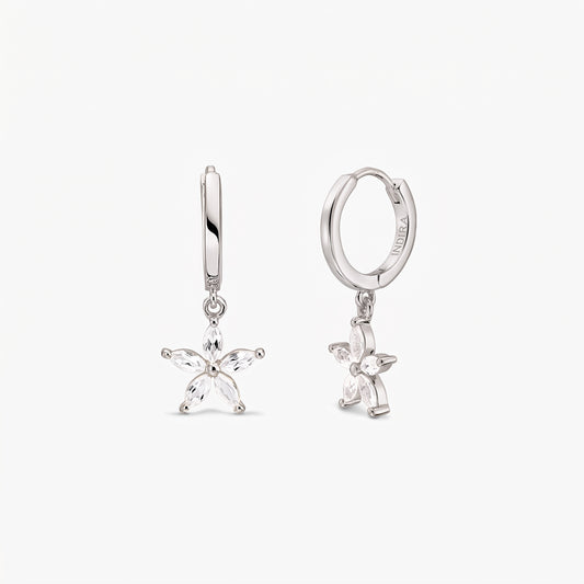 Pair of sterling silver huggie hoop earrings with dangling five-petal blossom charms set with white topaz on a white background.