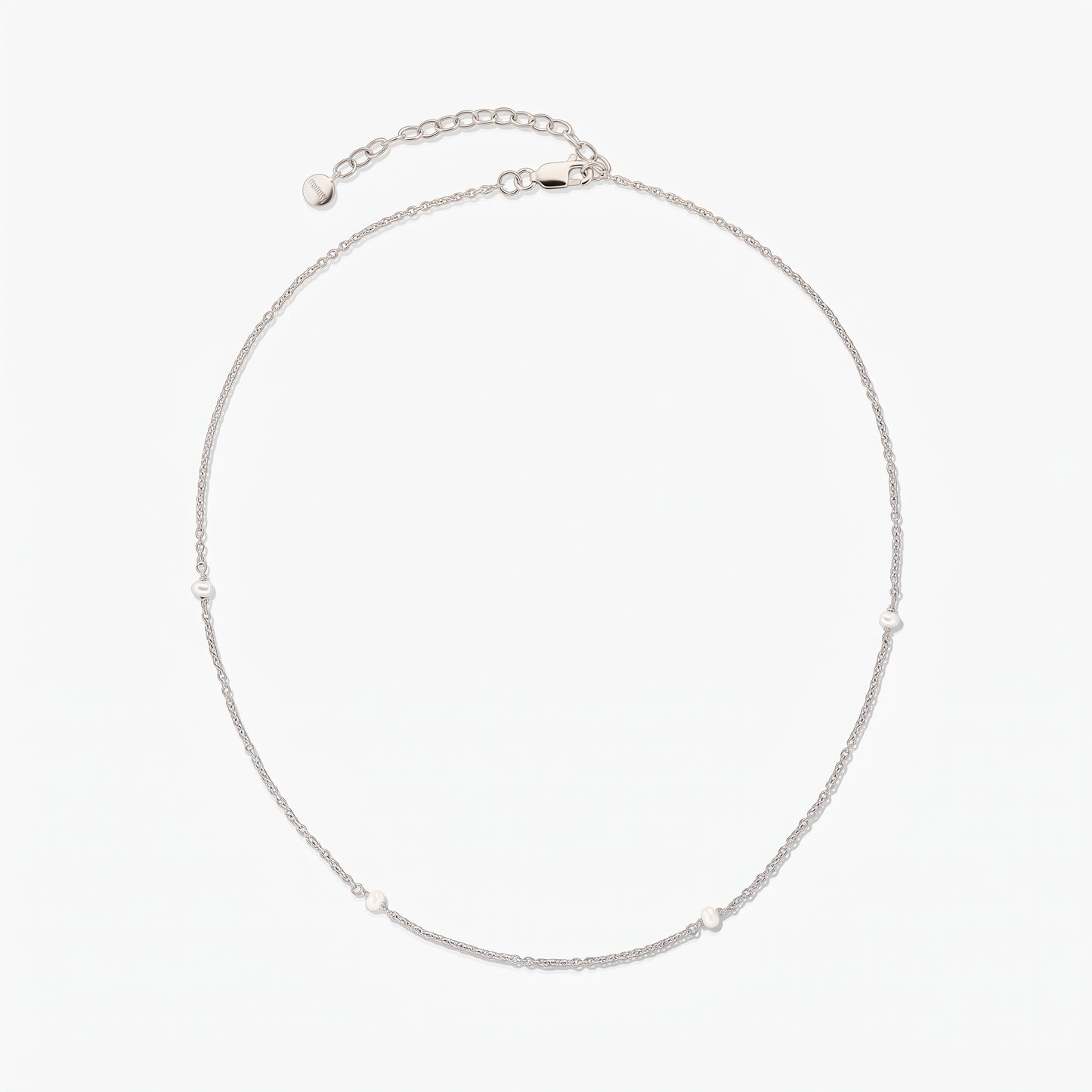 Collier chaîne en argent délicat avec de petites perles blanches espacées, présenté en cercle sur fond blanc avec une rallonge ajustable et un fermoir mousqueton.
